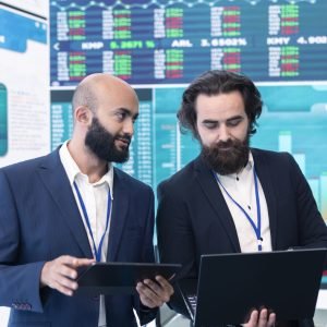 Diverse group of business specialists solve their daily tasks in control room with big screen, analyzing data numbers to ensure organizational progress. Startup management team.